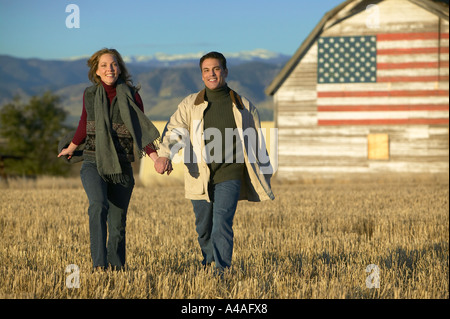 L uomo e la donna a piedi attraverso il taglio di erba Campi in autunno con fienile e bandiera americana Colorado Foto Stock