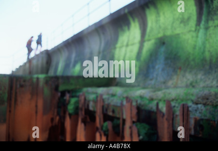 Impressionistica TENEBROSE FIGURE passaggi di arrampicata di calcestruzzo seawall con inutili arrugginiti e rotture di ferro per la difesa del mare in primo piano Foto Stock