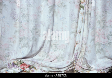 Dettaglio dall'esterno attraverso il vetro del malato-montaggio tende di grandi dimensioni con grande stampa floreale parte del quale è visibile sul davanzale Foto Stock