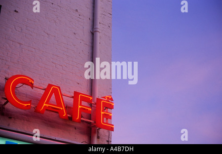 Dettaglio del neon rosso segno indicante CAFE sul lato della parete di mattoni dipinto di rosa e calorosamente incandescente sotto rosa-blu del cielo della sera Foto Stock