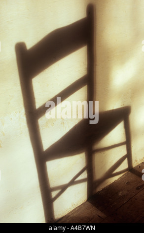 Ombra sul muro color crema con finestra irregolare riflessioni di semplice cucina in legno sedia intrecciati in un modo che inganna occhio Foto Stock