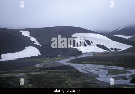 Un tipico paesaggio islandese grigio nero cloud rock bianco neve e acqua corrente foderato con vivido verde muschio Foto Stock