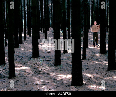 Un uomo legge un giornale mentre in piedi da solo in una foresta Foto Stock