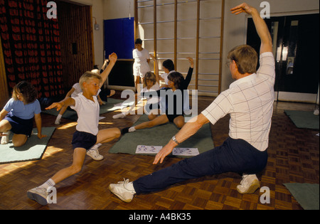 Insegnante che mostra esercizio sul tappeto per gli alunni durante la palestra classe NELLA SCUOLA PRIMARIA Foto Stock