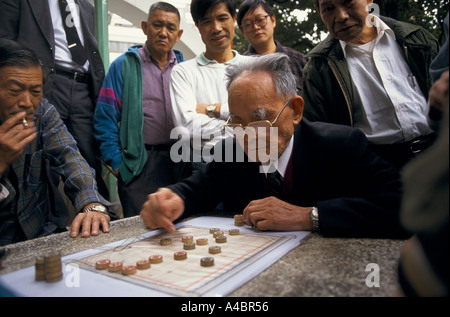 La gente di Hong Kong si sono riuniti intorno a guardare il vecchio uomo la riproduzione di bozze con avversario sulla strada Foto Stock