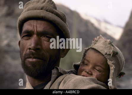 Baltistan, Pakistan, 1990; un pastore Balitsani porta il suo giovane figlio sulla sua schiena come egli cammina attraverso le montagne vicino a Skardu. Foto Stock