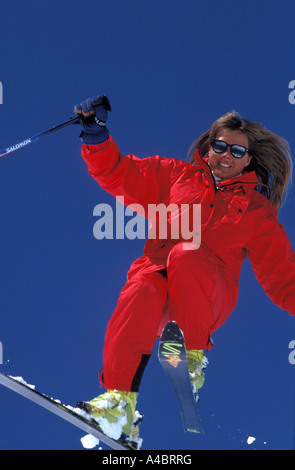 Sciatore femmina in un salto in alto che indossa un rosso brillante tuta da sci e giallo scarponi da sci Foto Stock