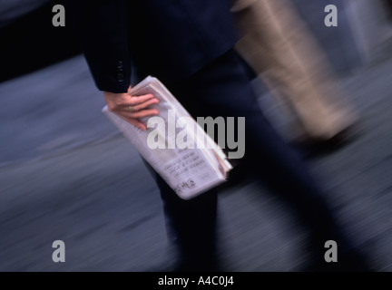 Ora di punta. A metà della sezione di un uomo d'affari che cammina con un vestito e una giacca andando in ufficio e portando un giornale ripiegato. La vita quotidiana in una città. Foto Stock