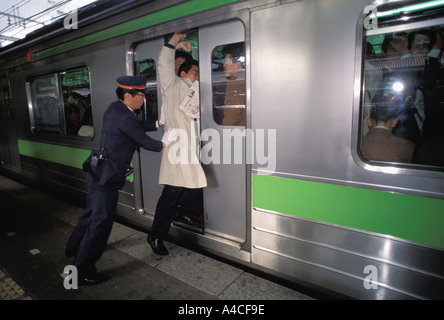 La gente che ottiene spinto in treno della metropolitana durante il Tokyo Rush Hour Foto Stock