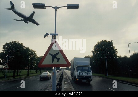 Aeromobile proveniente per atterrare all'aeroporto di Londra Heathrow vola su una strada principale molto trafficata passato un segno di avvertimento di bassa aeromobile in volo Foto Stock