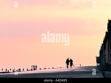 Le persone anziane a piedi dal mare al tramonto, Frinton on-Mare, Essex Foto Stock