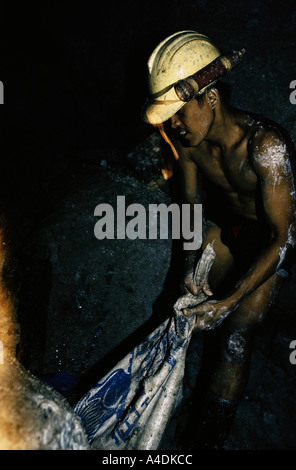 Un minatore in pantaloncini corti e un elmetto trascinando un sacco pieno di minerale di oro lungo un tunnel sotterraneo, Mount Diwata, sull isola di Mindanao Foto Stock