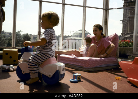 Un bimbo corse su un giocattolo push-bike come childminder gioca con un bambino, La Creche des Halles a Parigi, Francia Foto Stock