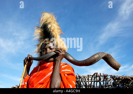 Un uomo Masai soffia in un corno di antilope in Masai Mara villaggio in Kenya. Foto Stock