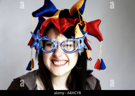 Giovane donna con giullari cappello e occhiali novità ridere Foto Stock