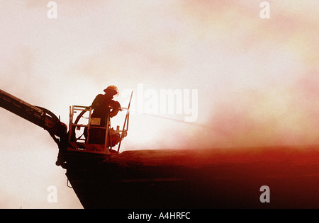 Fireman in culla a cherry picker la spruzzatura di un incendio nel tetto con acqua dal tubo flessibile Foto Stock