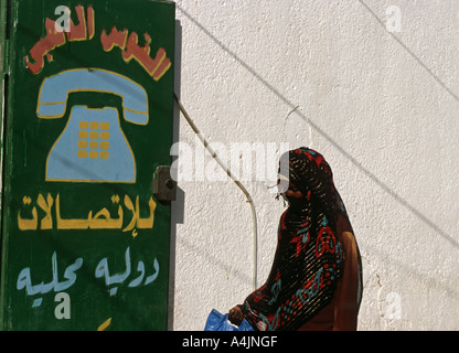 Donna con abito tradizionale nei pressi di un chiosco di telefono a Tripoli in Libia Foto Stock