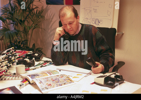 Art director con agenzia pubblicitaria o la casa editrice al banco parlando su due telefoni. Foto Stock