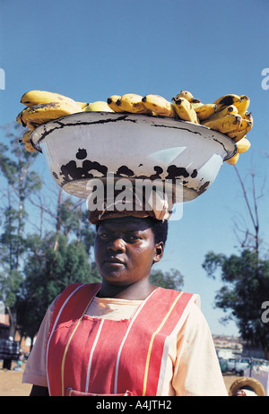 Nero donna africana che porta carico di testa di metallo grande ciotola di banane Soweto township vicino a Johannesburg in Sud Africa Foto Stock