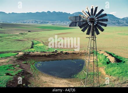 Mulino a vento pompa ad acqua azionata da un riempimento di una piccola diga in paese collinoso di Langeberge Provincia del Capo Sud Africa Foto Stock