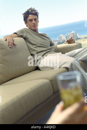 Uomo seduto sul divano azienda bere Foto Stock