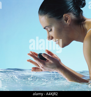 Donna in acqua holding pietre in mani con gli occhi chiusi, vista laterale Foto Stock