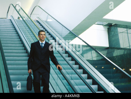 Imprenditore cavalcare giù escalator Foto Stock
