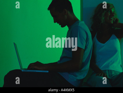 Uomo con notebook, donna seduta dietro di lui Foto Stock