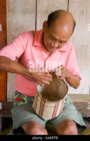 Un uomo Bidayuh mette la rifinitura di un cesto tessuto in corrispondenza di una casa lunga a Annah Rais nel Sarawak Foto Stock