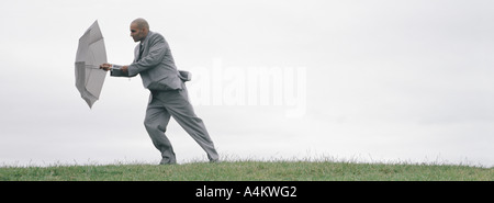 Uomo che cammina nel vento con ombrello aperto lo schermatura a piena lunghezza Foto Stock