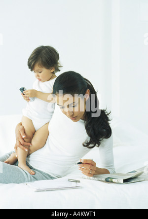 Giovane donna puntellato sul gomito tenendo la penna con una mano, tenendo bambina con altro braccio Foto Stock