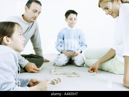 Ragazzo e una ragazza con i genitori la riproduzione di domino sul pavimento Foto Stock