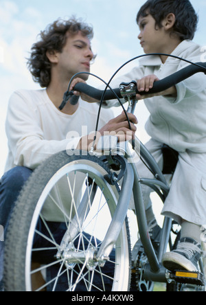 Ragazzo sulla bicicletta guardando al padre di tenere su bicicletta, a basso angolo di visione Foto Stock