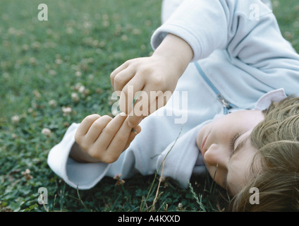 Ragazzo che giace sull'erba tenendo le dita insieme nella parte anteriore del viso Foto Stock