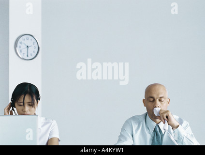 Executive telefono tenendo premuto contro la bocca, gli occhi chiusi, assistente lavorando accanto a lui Foto Stock