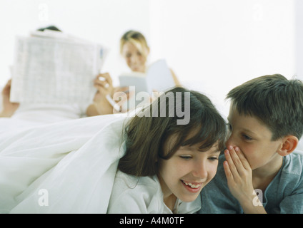 Ragazzo sussurra a ragazza, i genitori la lettura in background Foto Stock