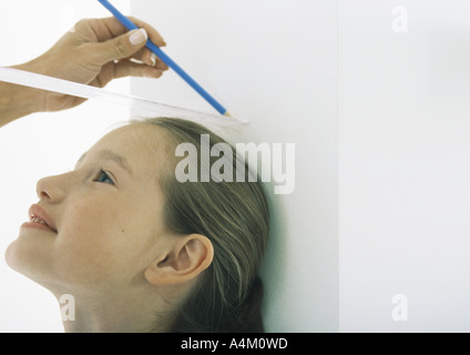 La ragazza con la testa contro la parete essendo misurata da donna Foto Stock