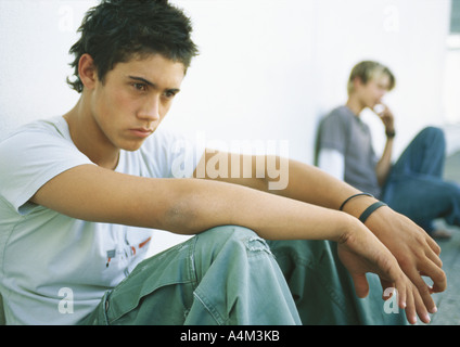 Giovane uomo seduto a terra, adolescente in background Foto Stock