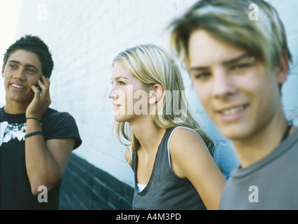 I giovani in piedi accanto alla parete, uno tramite telefono cellulare Foto Stock