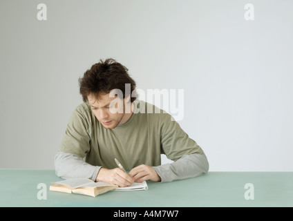 Giovane uomo seduto con libro aperto, prendere appunti Foto Stock