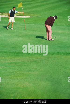 Giocatore di golf putting mentre il secondo uomo detiene golf bandiera Foto Stock