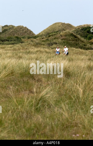 Due ciclisti attraversando l'erba dune di Est Frisone Isola di Langeoog Foto Stock