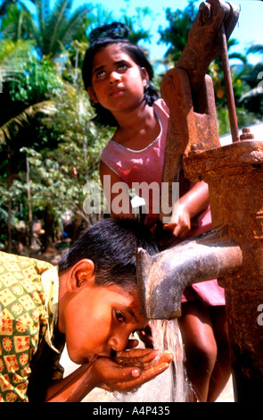 Ragazza giovane pompe acqua bene per il fratello Bangladesh rurale Foto Stock