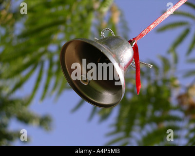 Campana di argento è appeso a un filo rosso da un albero con il blu del cielo Foto Stock