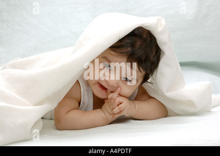 ANG77643 giovani South Asian Indian bambina di quattro mesi di età che giace sulla pancia mettendo il dito in bocca un panno bianco sulla testa India Foto Stock