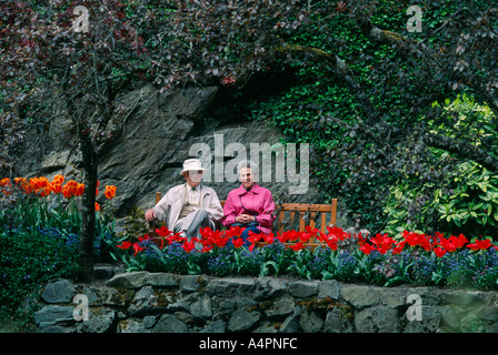 Coppia senior in appoggio sul banco di lavoro ai Giardini Butchart in primavera Foto Stock
