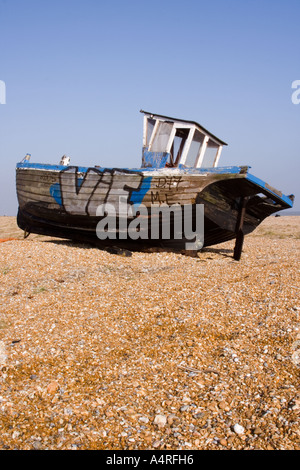 Un abbandonato la pesca in barca si siede decadendo sulla spiaggia di ciottoli di Dungeness in Kent verticale. Foto Stock