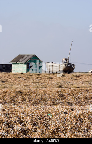 Abbandonata la pesca in legno barca accanto ad un verde abbandonati capanna sulla spiaggia di ciottoli a Dungeness nel Kent. Foto Stock