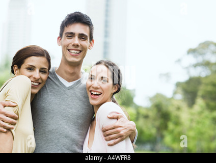 Giovane uomo in piedi con le braccia intorno a due giovani donne nel parco urbano Foto Stock