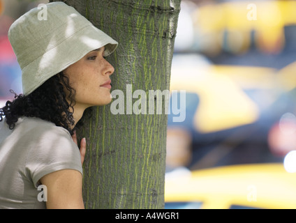 Giovane donna in piedi accanto ad albero Foto Stock